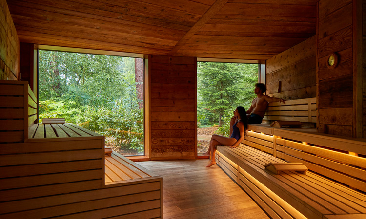 Couple sitting in a Nordic Sauna with views out to the surrounding forest.