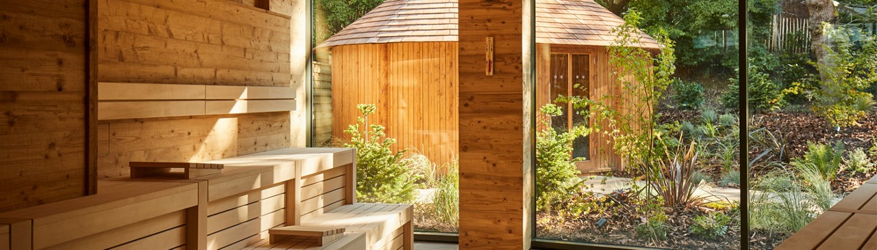 Inside of wooden sauna looking out to a forest garden where a Scandinavian Snug sits.