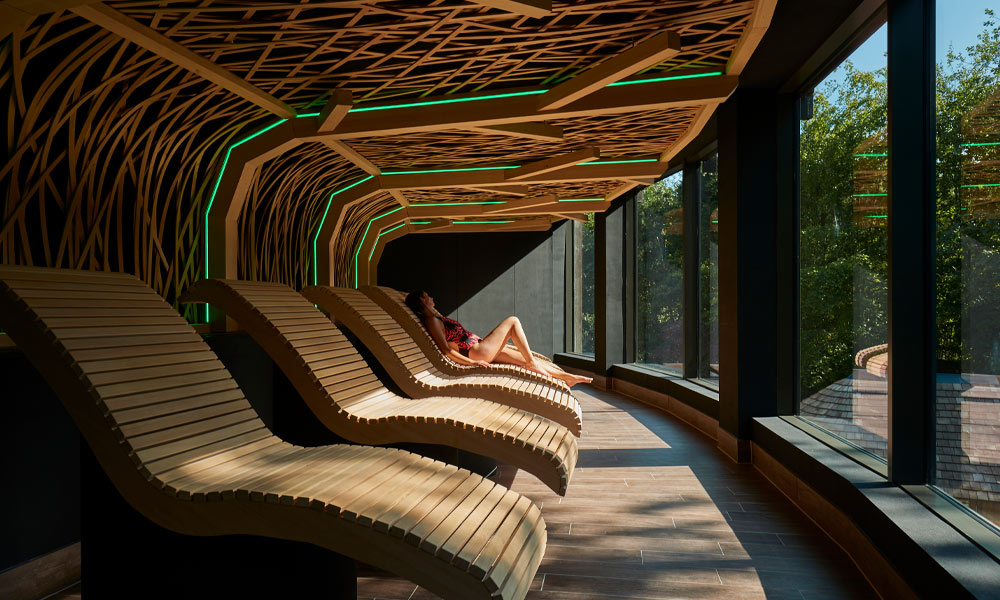 Woman laying on a wooden contoured seat looking out to the forest.