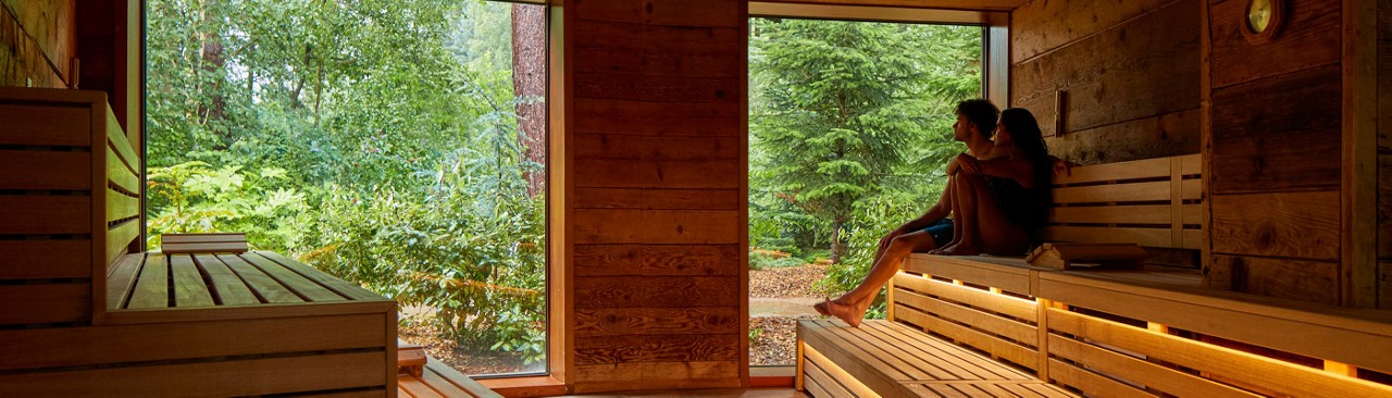 Aman and woman sitting inside the Nordic Sauna, taking in the forest views.