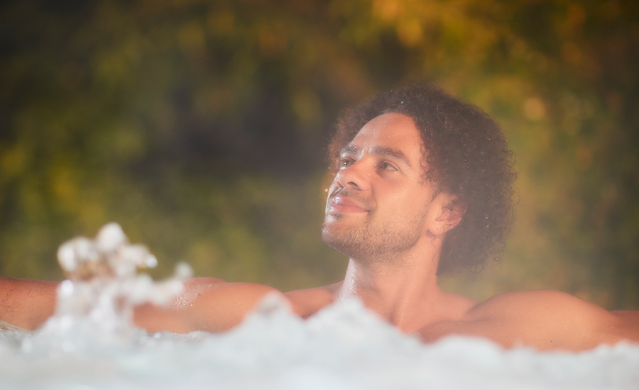 A man soaking in a steamy outdoor hot tub.