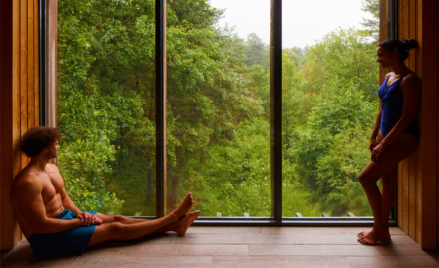 Man and a women inside the Treetop Sauna with panoramic views of the forest.