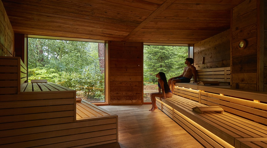 Man and woman sitting enjoying the forest views from inside the Nordic Sauna.