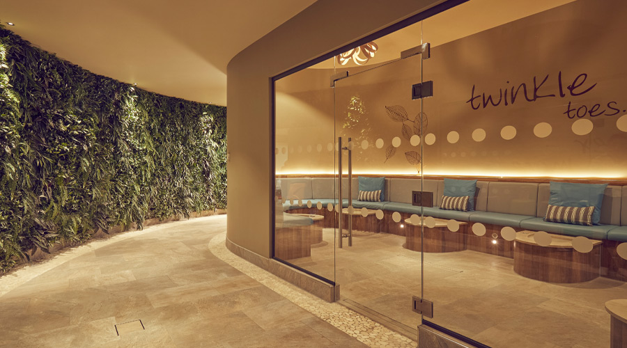 Hallway with a foliage wall and views into the Sole Therapy rool with individual footbaths and comfortable bench seating.