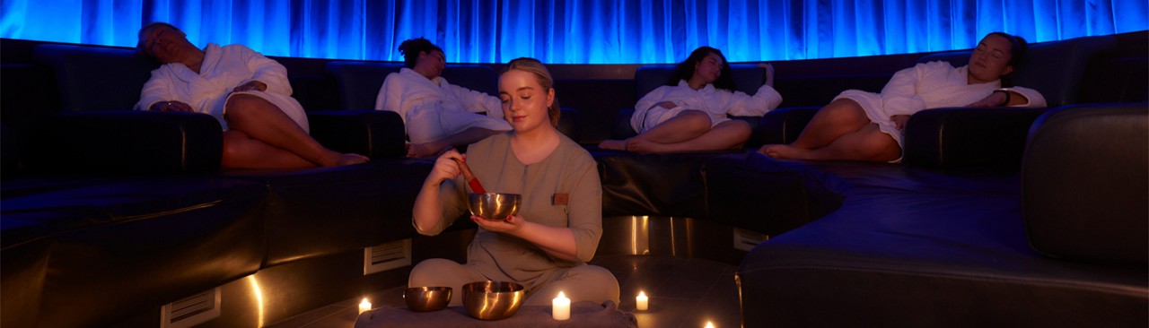 Woman sitting in front of metal bowls whilst people sleep in the background.