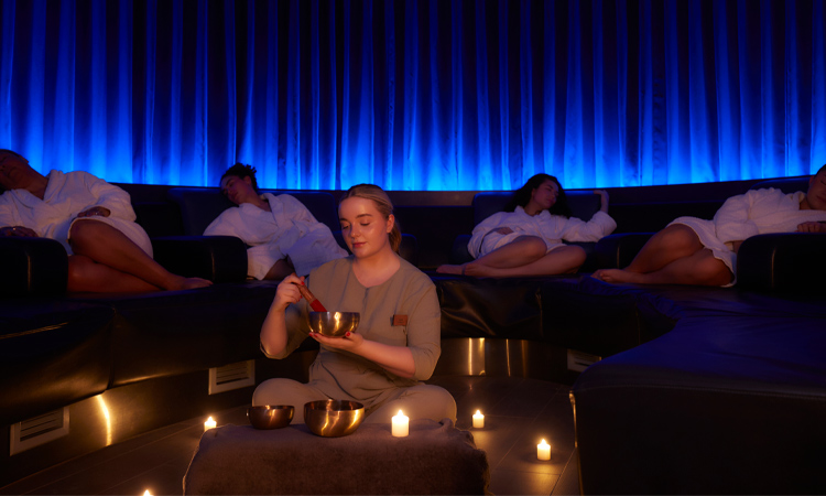 Woman holding a metal bowl whilst people sleep on comfortable chairs. 