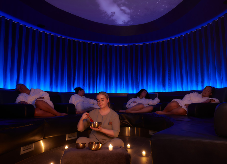 Woman holding a metal bowl whilst people sleep on comfortable chairs. 