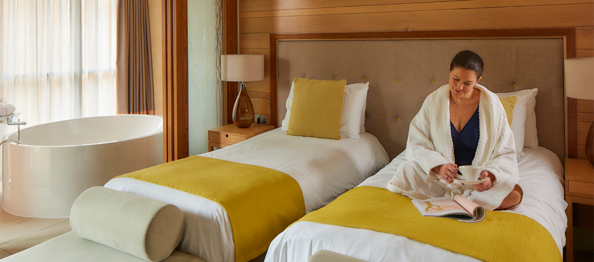 Woman sitting on a twin bed in a Spa Suite reading a book.