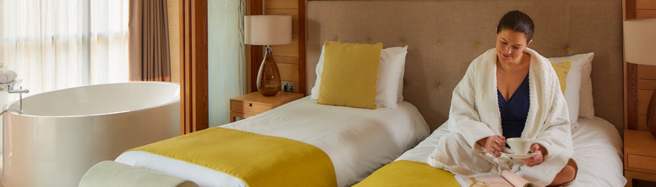 Woman sat on a bed in a twin bed spa suite reading a book
