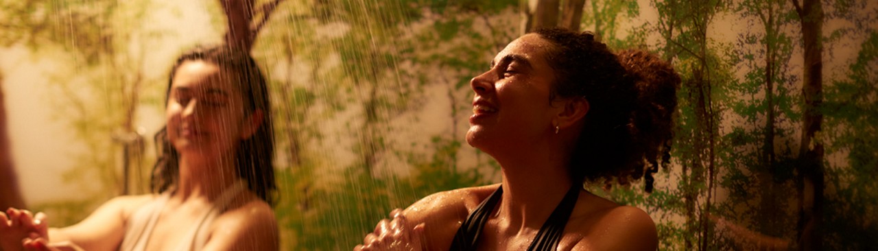 Two women soaking in a rain forest themed shower.