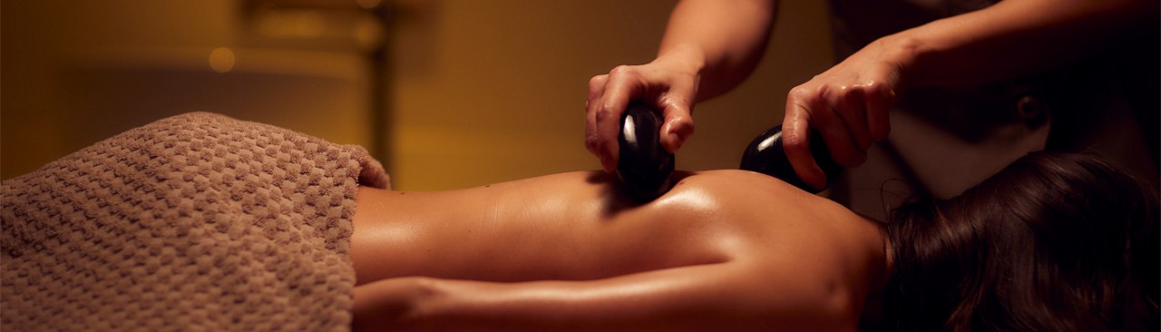 Woman laying having hot stones massaged across her back.