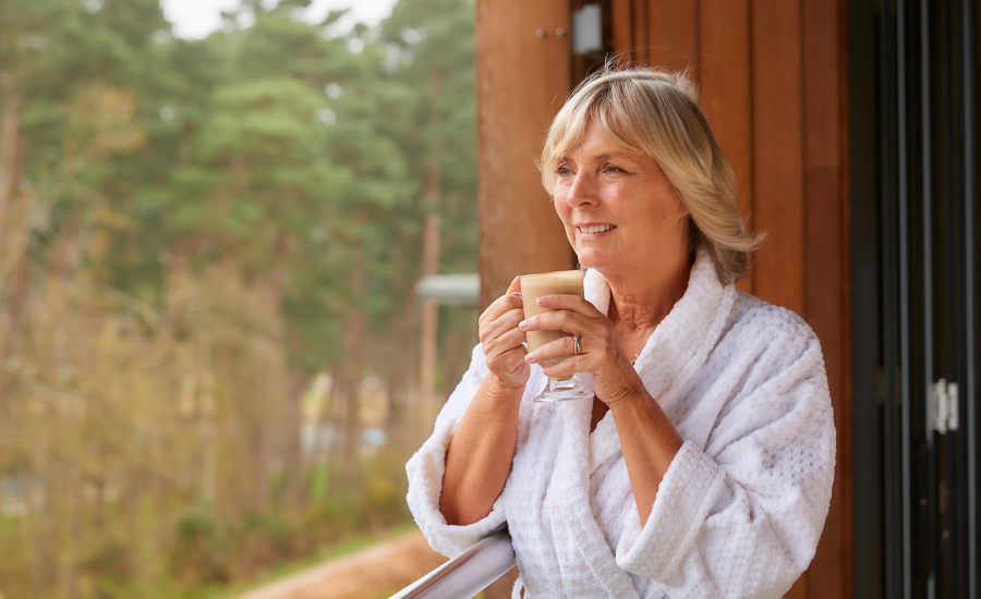 Woman holding a coffee as she looks out to the forest from a Spa Suite.